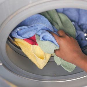 A close-up of a hand loading colorful towels into a front-loading washing machine.